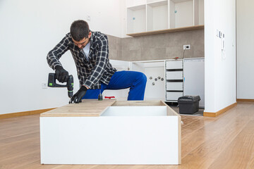 Wall Mural - Carpenter screwing screws and assembling parts of kitchen with electric screwdriver