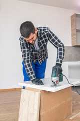 Wall Mural - A carpenter with a corded jigsaw cutting a part of the wooden surface (board)