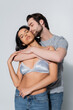 © LIGHTFIELD STUDIOS - young man hugging sexy girl in satin bra standing with closed eyes on grey.