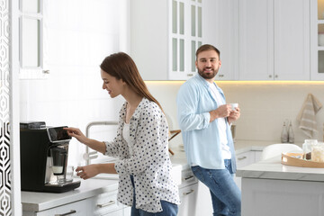 Wall Mural - Beautiful young woman and her boyfriend using modern coffee machine in kitchen