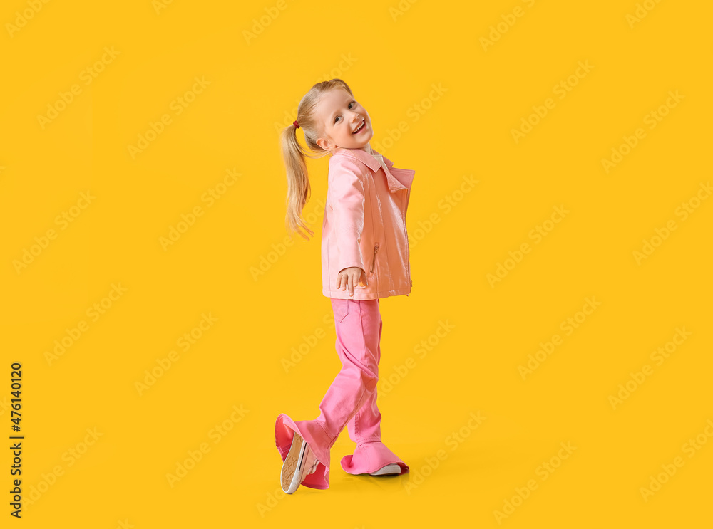 Cute little girl in pink jacket dancing on yellow background