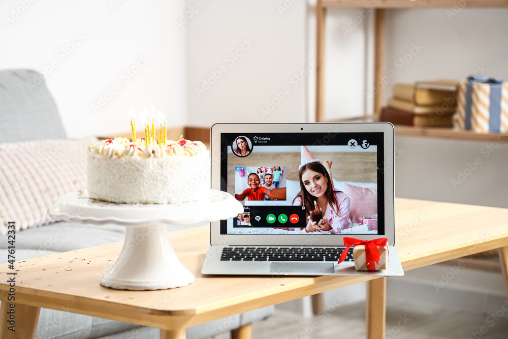 Laptop, gift and cake on table in room. Celebrating birthday online due to coronavirus epidemic