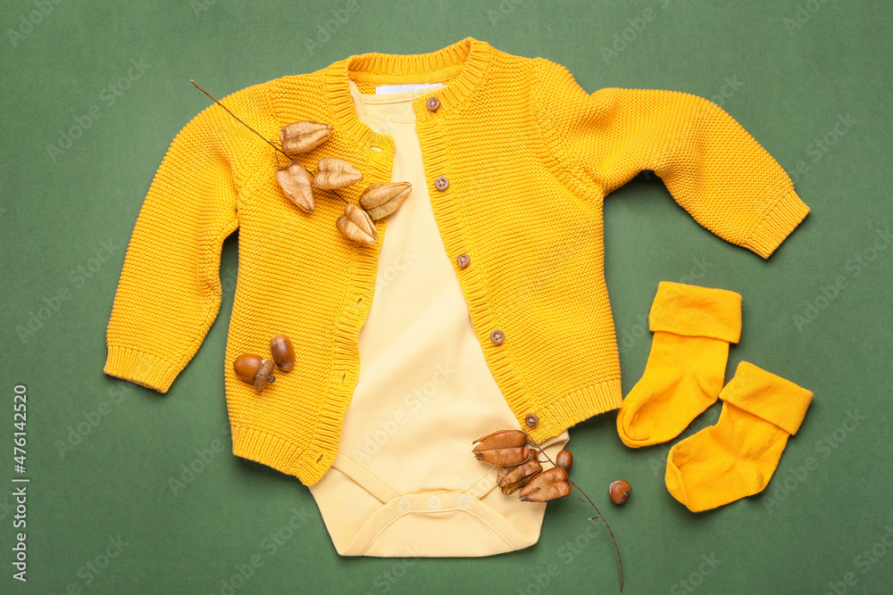 Stylish baby clothes and natural decor on green background