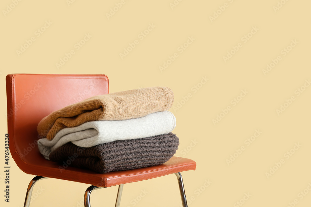Stylish winter clothes on chair against color background