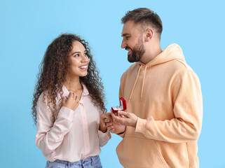 Wall Mural - Young man proposing to his girlfriend on color background