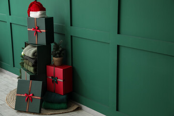 Gift boxes with winter sweaters and Santa hat near green wall in room