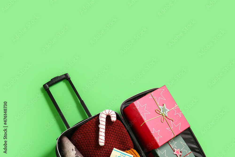 Open suitcase with Christmas gift boxes and clothes on green background