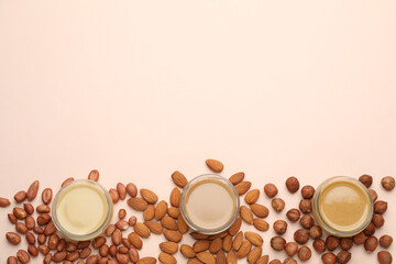 Different types of delicious nut butters and ingredients on beige background, flat lay. Space for text