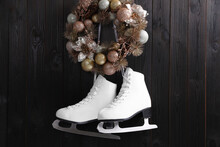 Pair Of Ice Skates And Beautiful Christmas Wreath Hanging On Dark Wooden Wall