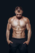 © satyrenko - Muscular and fit young bodybuilder fitness male model posing standing with his head down over black background