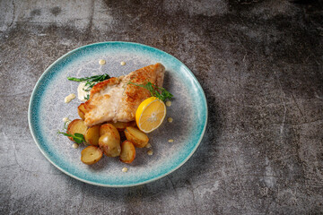 Canvas Print - Serving a dish from a restaurant menu. Baked Trout steak with lemon, salad and dill and parsley greens on a plate against a gray stone table