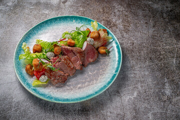 Canvas Print - Serving a dish from the restaurant menu. Meat fried al dente (Semi-cooked) with vegetables, green salad and croutons on a plate against the background of a gray stone table, a delicious appetizer