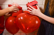 A Boy In A Red T-shirt And A Girl In A Black Dress Give Each Other Gifts For Valentine's Day With Red Balls In The Form Of Hearts