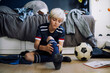 © Maskot - Blond boy wearing sock while sitting in bedroom at home
