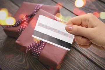 Sticker - Young woman holding a credit card and a gift box against the background of Christmas decor, shopping on the Internet,