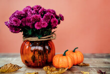 Two Small Decorative Pumpkins And A Vase With Chrysanthemums On A Wooden Table. Preparation For The Halloween Holiday.