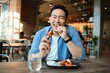 © Mallika - Happy  Asian man eating BBQ chicken wings in restaurant.