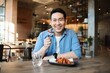 © Mallika - Happy  Asian man eating BBQ chicken wings in restaurant.