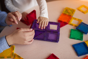 Crop mother with daughter playing with magnetic tiles