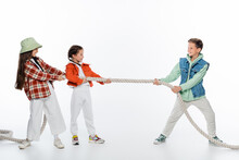 Side View Of Cheerful Girls Pulling Rope While Playing Tug Of War Game With Boy On White.