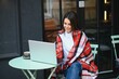 © Serhii - Young freelancer woman enjoying coffee while working outdoors on a laptop computer connected to public Wi-Fi. Stylish student girl studying online in city.