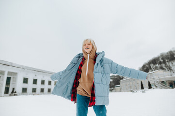 Wall Mural - Portrait of happy woman in warm clothes in snow on winter street background having fun with smile on face posing at camera.