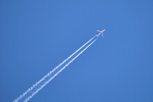 Distant Passenger Jet Plane Flying On High Altitude On Clear Blue Sky Leaving White Smoke Trace Of Contrail Behind. Air Transportation Concept