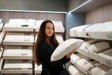 Cheerful Brunette Lady Choosing New Pillow While Standing In Bedding Store