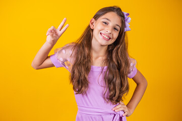 Photo of a charming and delicate preteen girl making a V sign smiling isolated on yellow background.