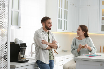 Poster - Young man talking with his girlfriend while using modern coffee machine in kitchen