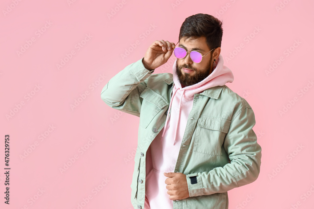 Handsome man in stylish sunglasses and jacket on pink background