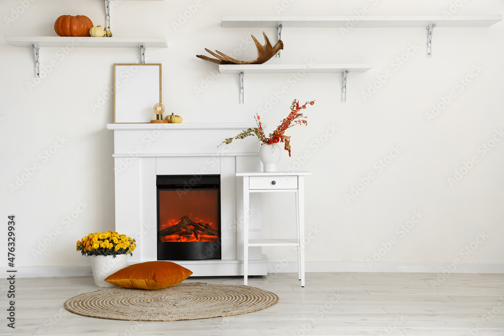 Interior of light room with modern fireplace, blank frame and vases