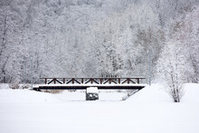Park After Snowfall, View To Wooden Bridge Over The Frozen Lake. Snow Covered Trees In Winter, Picturesque Landscape