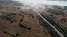 Aerial Panoramic View Of An Intercity Road Between Green Trees With White Fog Clouds Over It. Beautiful Morning Landscape.