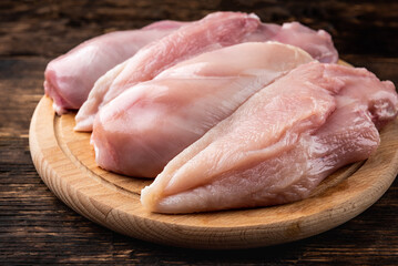 Wall Mural - Raw chicken fillets on wooden board on dark wooden background.