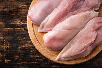 Wall Mural - Raw chicken fillets on wooden board on dark wooden background.