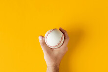 Male Hand Holds A Baseball Ball On Yellow Background.