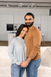 © Vadim Pastuh - Smiling man hugging his charming woman. Two people standing and joyfully looking at the camera. Young Indian couple happily spending time in cozy modern kitchen at home