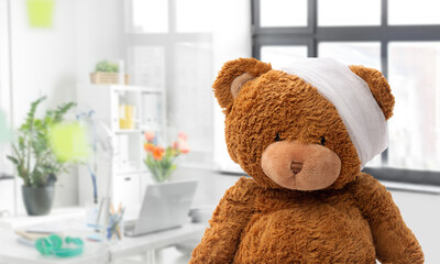 Wall Mural - medicine, healthcare and childhood concept - teddy bear toy with bandaged head over medical office at hospital background