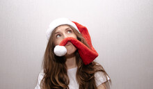 Portrait Of A Young Brunette Girl Wearing Santa Claus Santa Hat Fooling Around And Holding Pompom Caps Over Her Lip