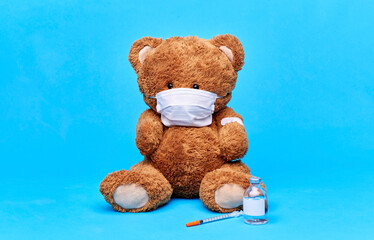 Wall Mural - vaccination, healthcare and pandemic concept - teddy bear toy in protective medical mask with patch on paw, vaccine and syringe over blue background