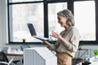 © LIGHTFIELD STUDIOS - Side view of positive businesswoman having video call on laptop near model of building in office.