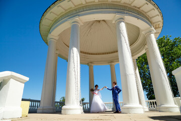 Bride and groom in gazebo near the white columns in a sunny summer day in the city park