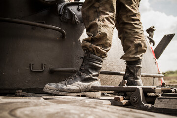 Legs of a soldier standing on metal tank, on a battlefield. Wearing military boots and woodland camo pants (camouflage trousers).