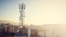 Close-up View From A Drone Of A Telecommunications Tower With Cellular Network Antennas 4G, 5G Against The Background Of The City At Sunset. Banner