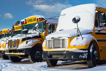 Snow covered school buses parked in a school parking lot.