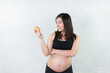Asian pregnant woman holding an apple on gray background, healthy food and people concept. Happy pregnant woman eating red apple.