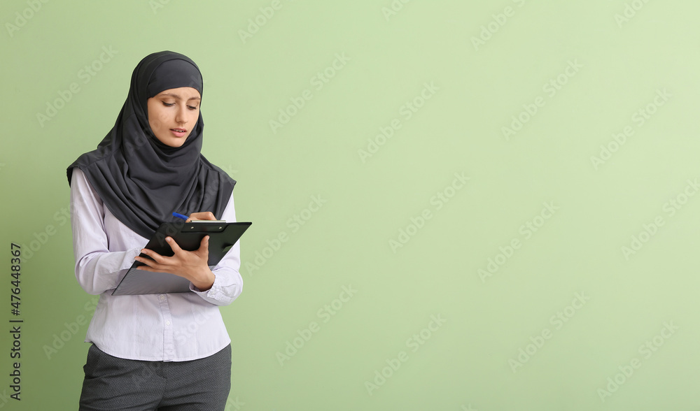 Muslim secretary with clipboard on color background