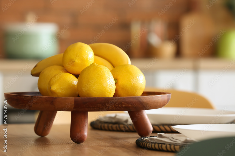 Stand with fresh bananas and lemons on dining table in kitchen, closeup