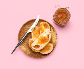 Glass jar of tasty pear jam and bread on pink background